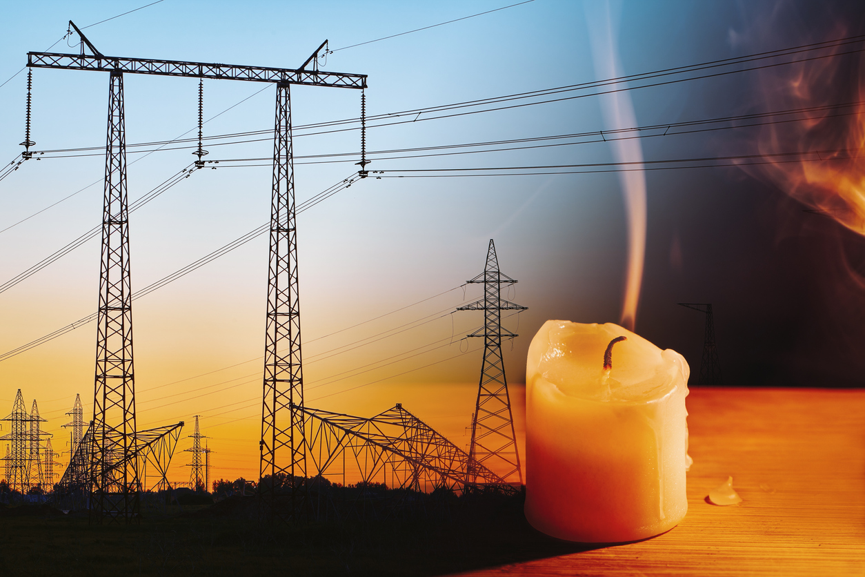 Electric power transmission towers at sunset with a melting candle in the foreground, symbolizing power outage.