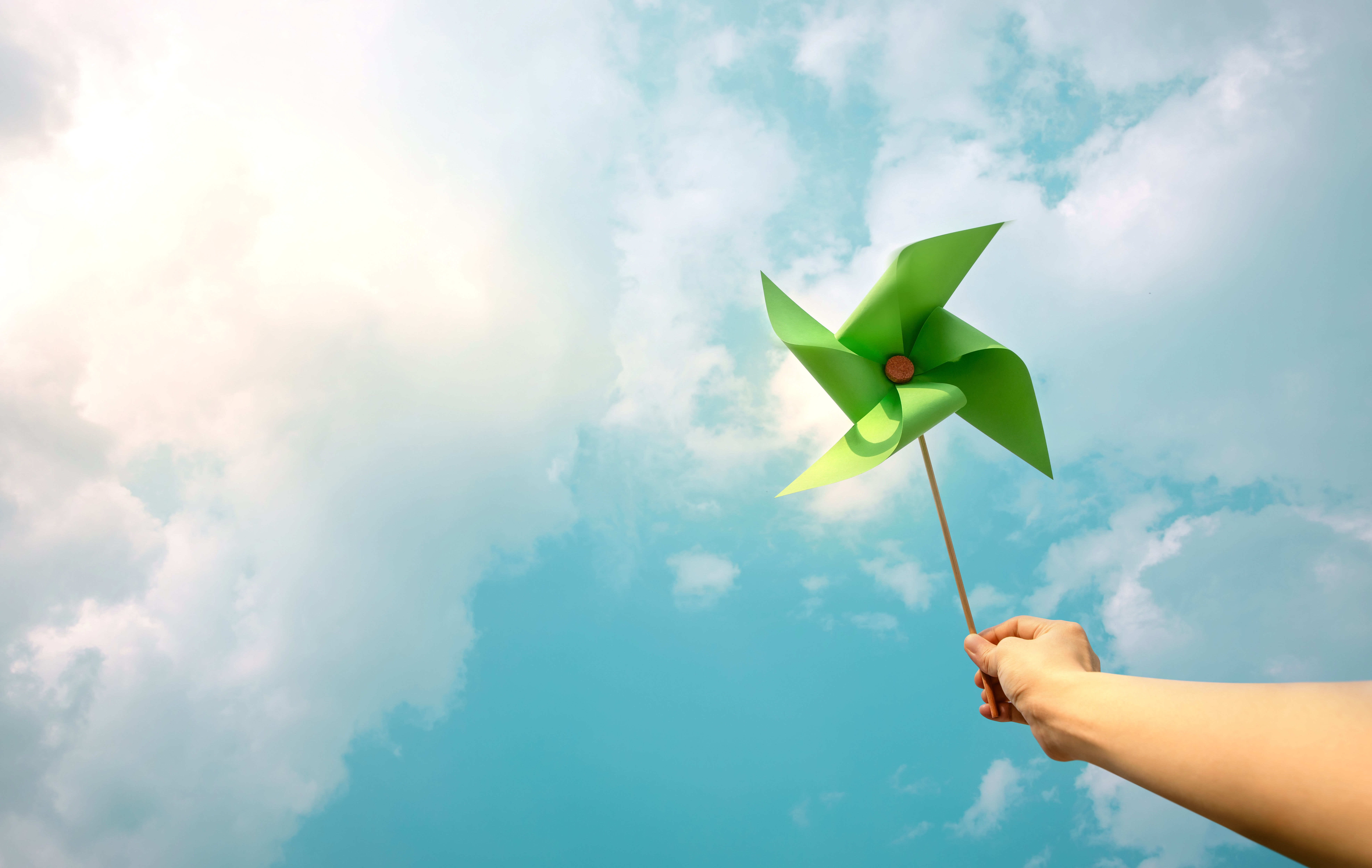 Hand holding a green pinwheel aloft against a clear blue sky