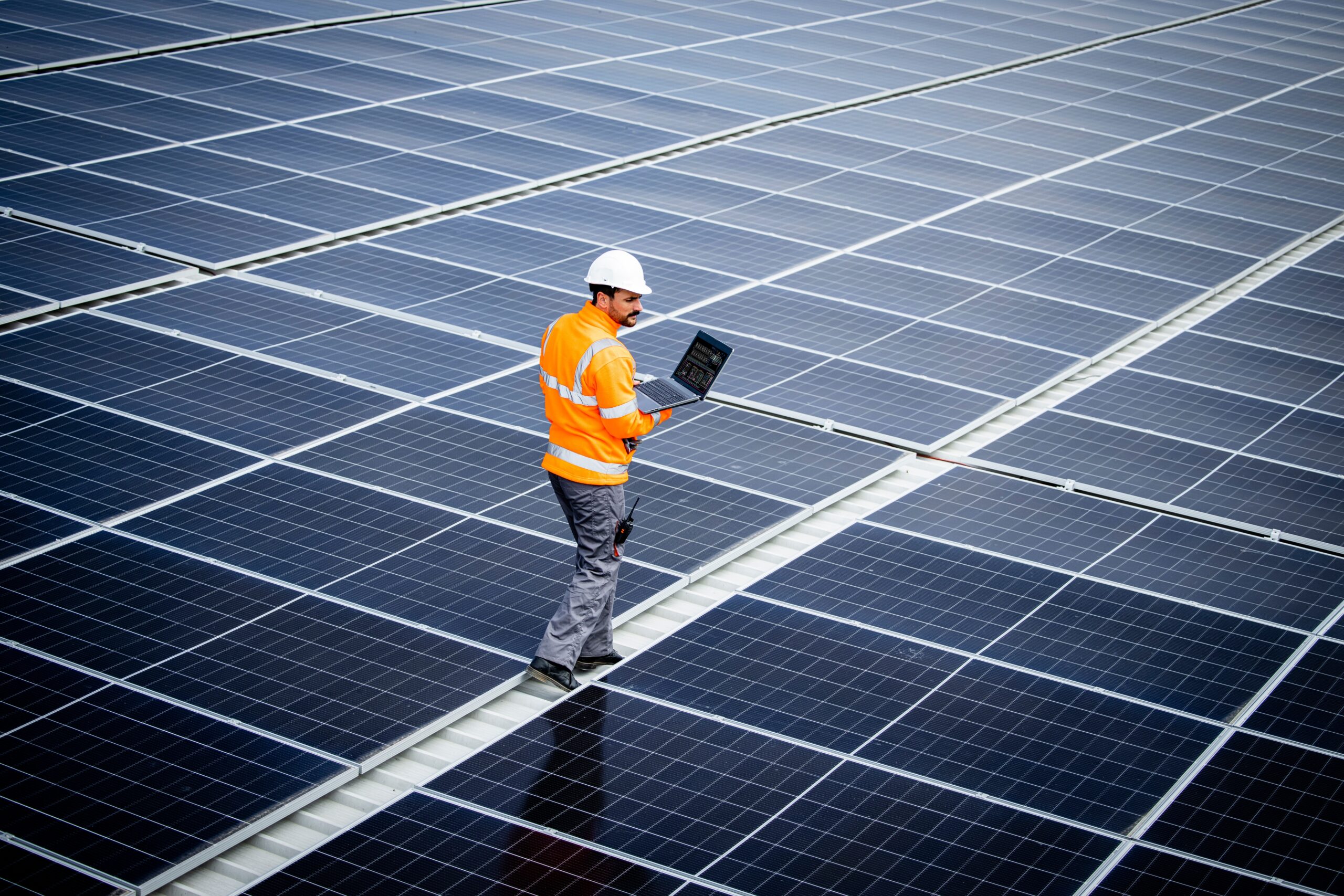 Engineer inspecting solar panels with a laptop at a solar power plant.
